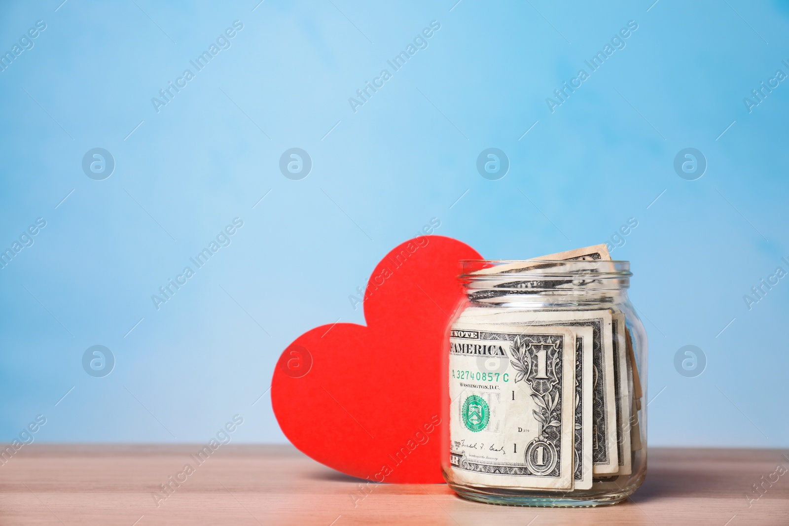 Photo of Red heart and donation jar with money on table against color background. Space for text