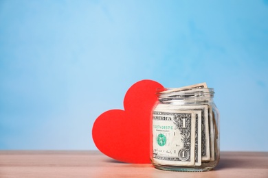 Photo of Red heart and donation jar with money on table against color background. Space for text