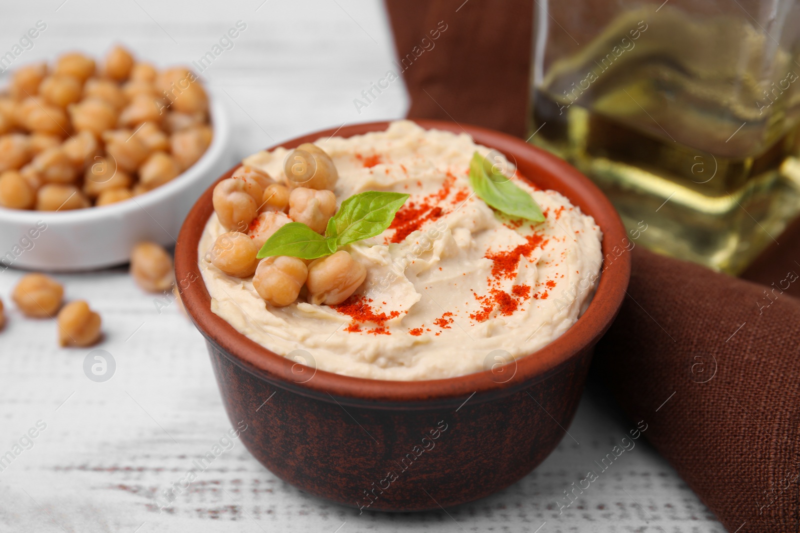 Photo of Delicious hummus with chickpeas and paprika served on white wooden table, closeup