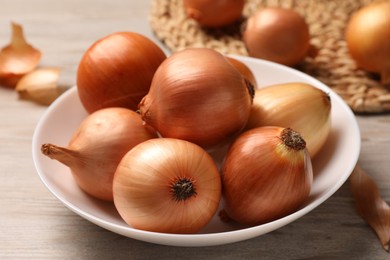 Photo of Bowl with many ripe onions on wooden table