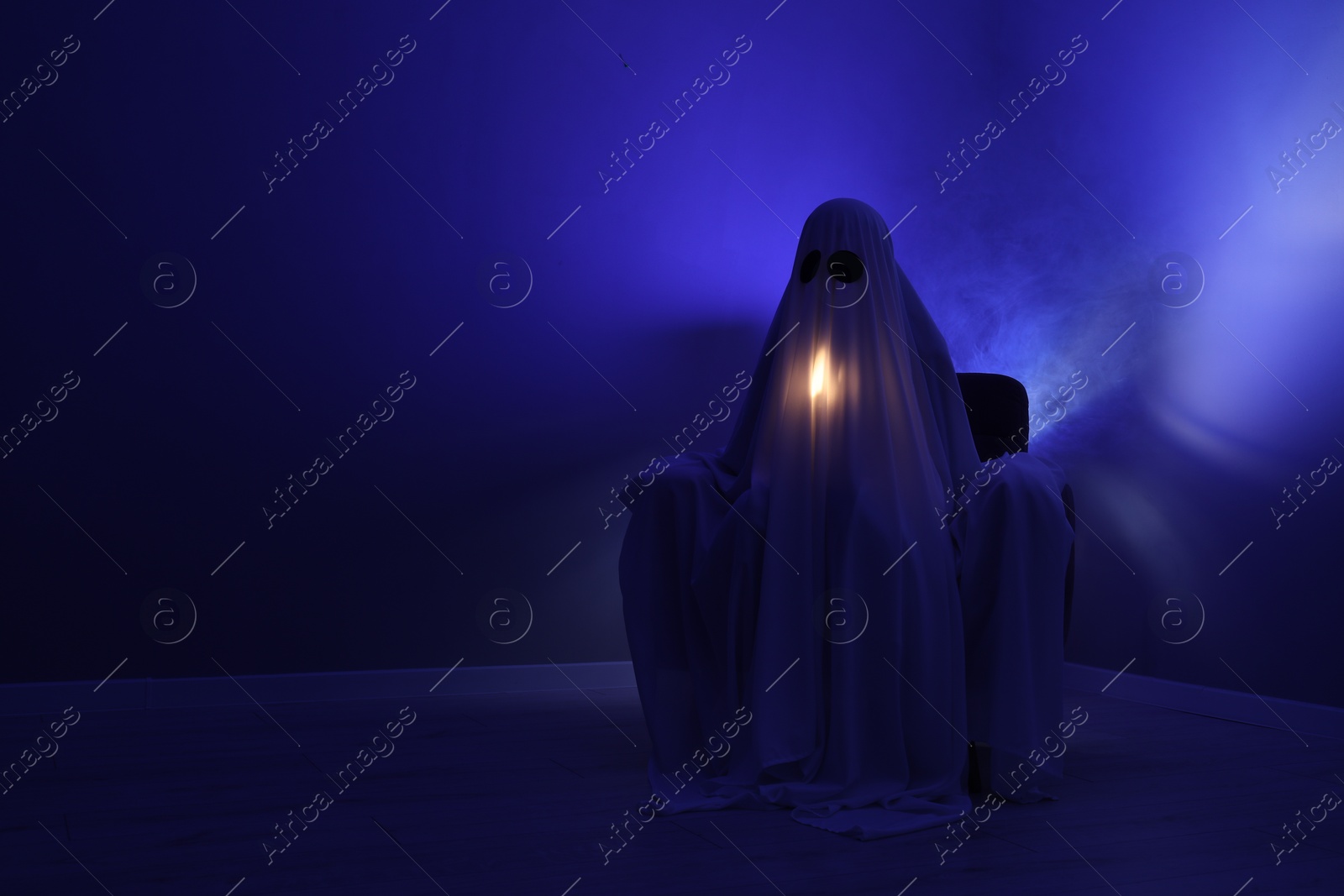 Photo of Creepy ghost. Woman covered with sheet sitting in armchair in blue light, space for text