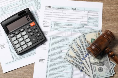 Tax return forms, dollar banknotes, calculator and gavel on wooden table, top view