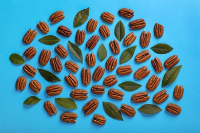 Flat lay composition with tasty pecan nuts and green leaves on light blue background