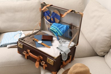 Open suitcase with different men clothes and accessories on sofa