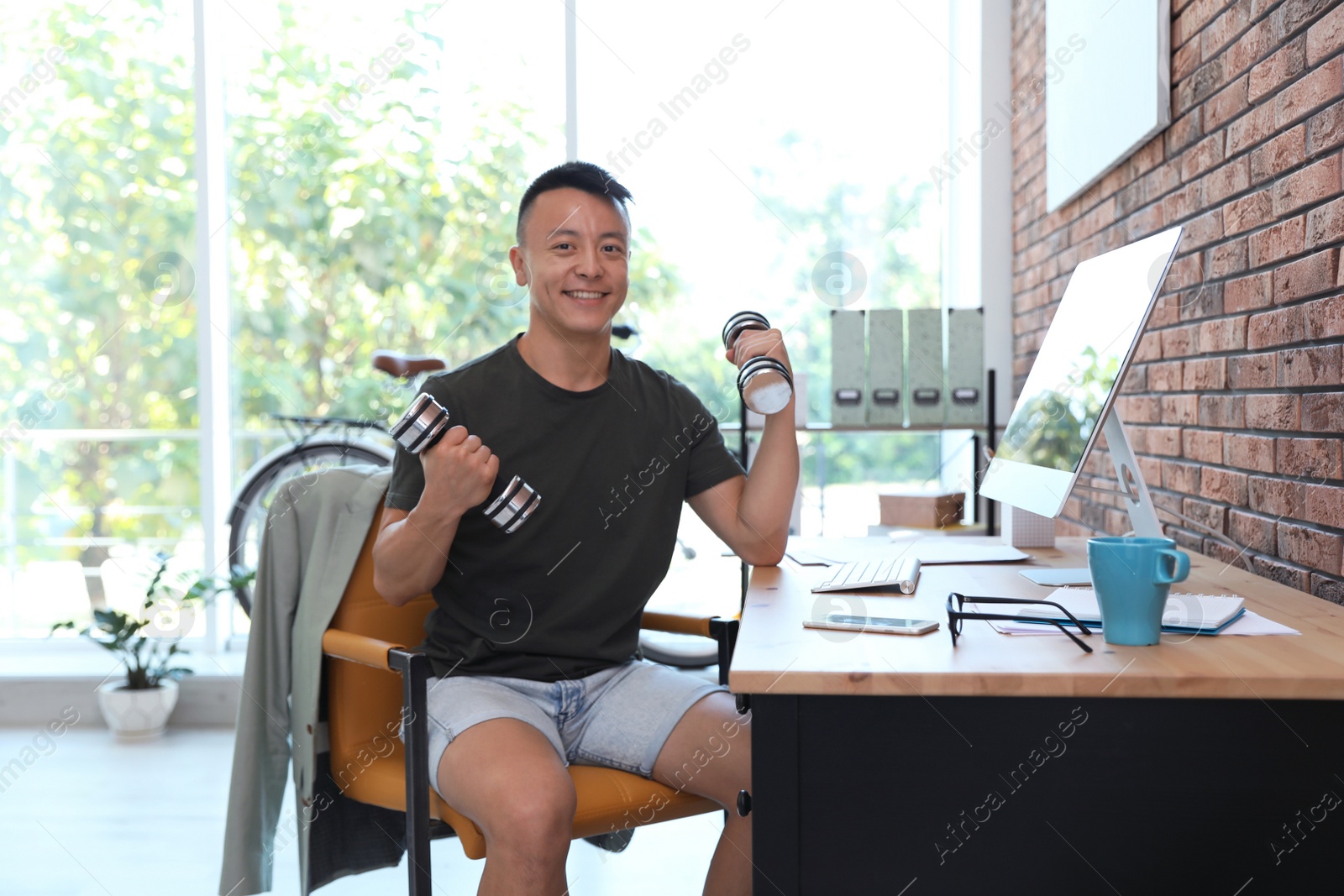 Photo of Young man lifting weights in office. Workplace fitness