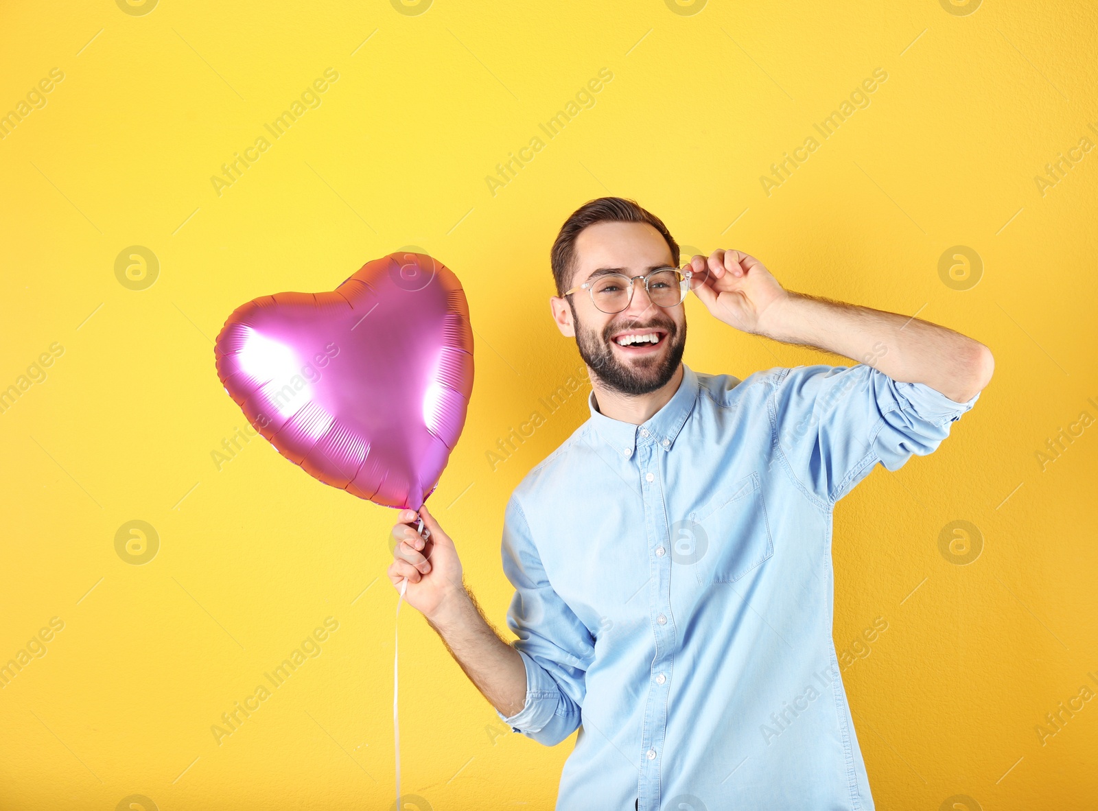 Photo of Portrait of young man with heart shaped balloon on color background