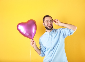 Portrait of young man with heart shaped balloon on color background