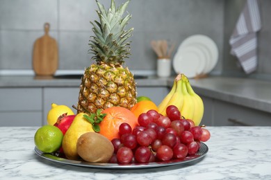 Plate with different ripe fruits on white marble table in kitchen