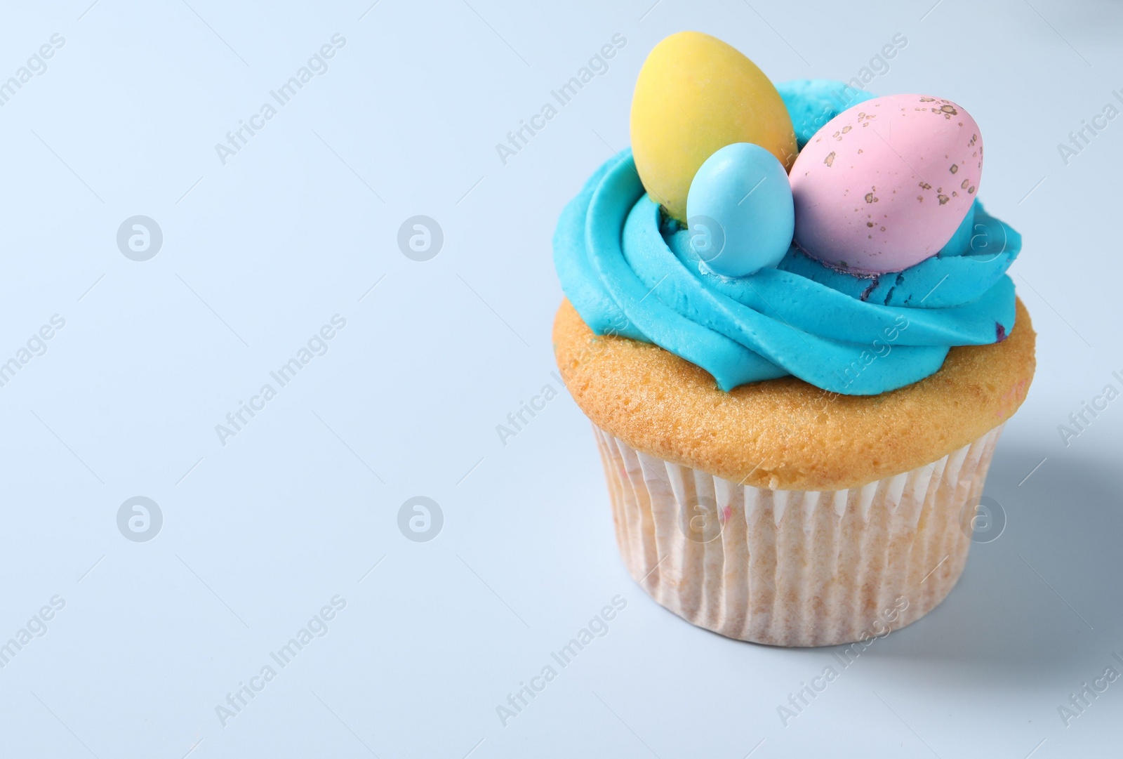 Photo of Tasty decorated Easter cupcake on light blue background. Space for text