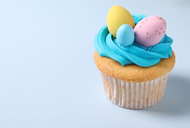 Photo of Tasty decorated Easter cupcake on light blue background. Space for text