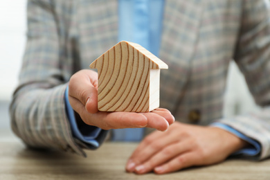 Real estate agent holding house figure at wooden table, closeup