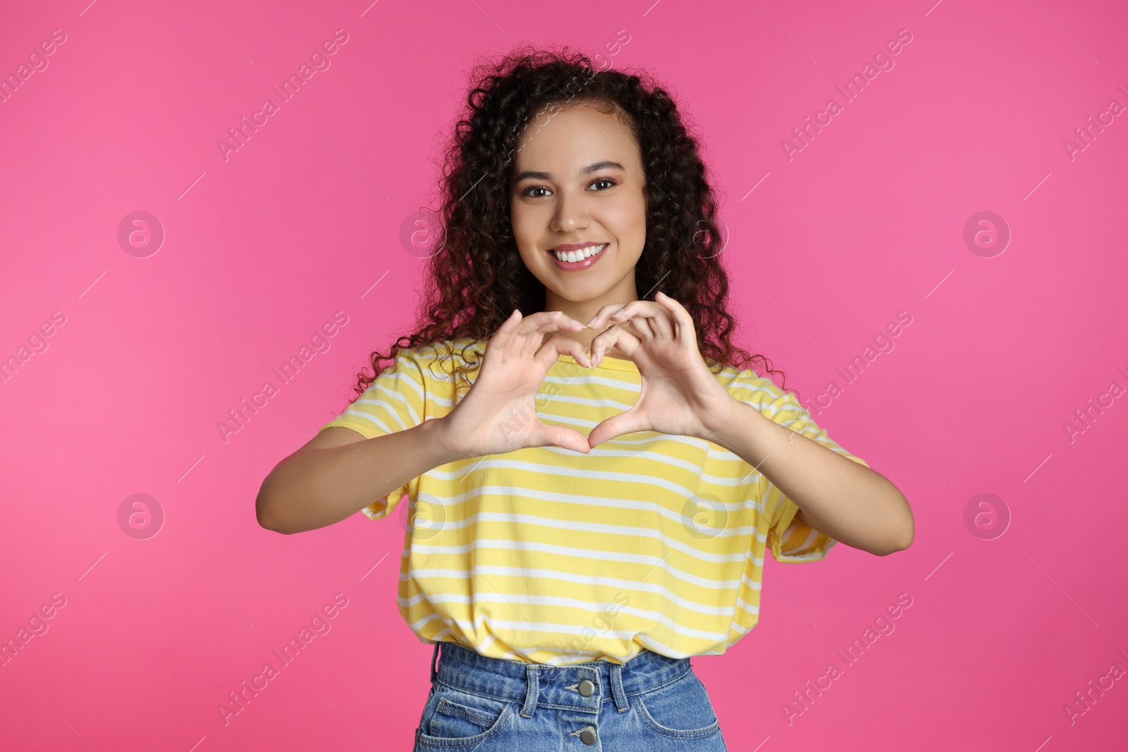 Photo of Happy young African-American woman making heart with hands on pink background