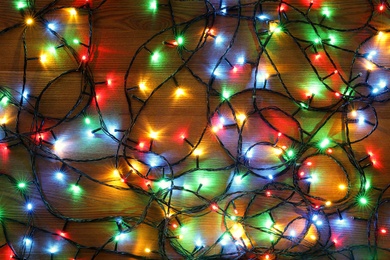 Colorful Christmas lights on wooden table, top view