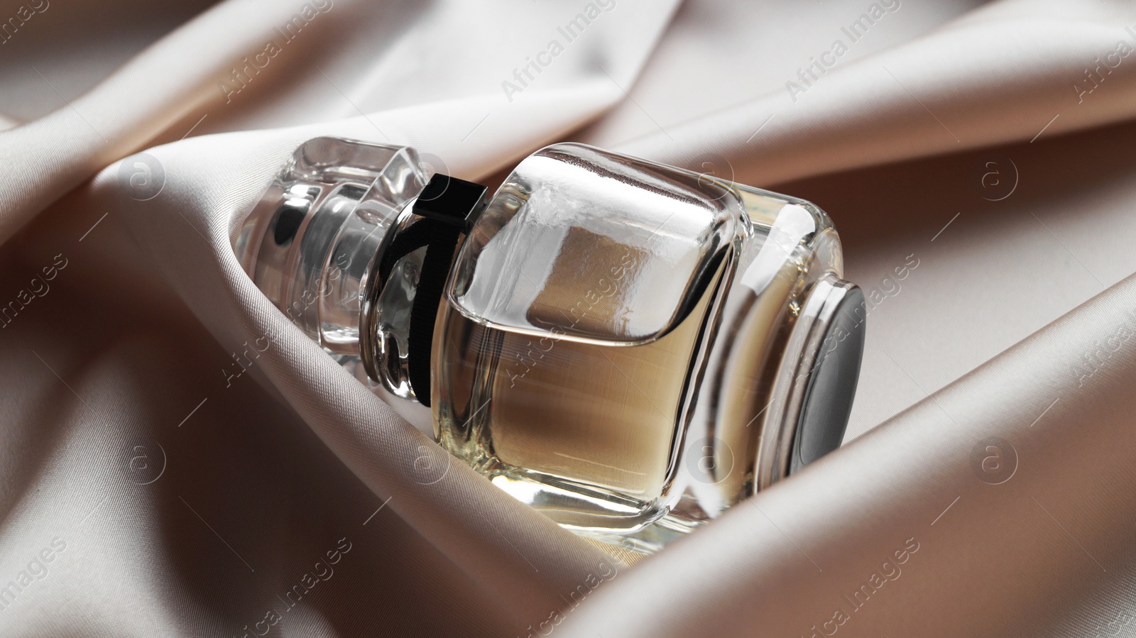 Photo of Luxury bottle of perfume on beige silk, closeup