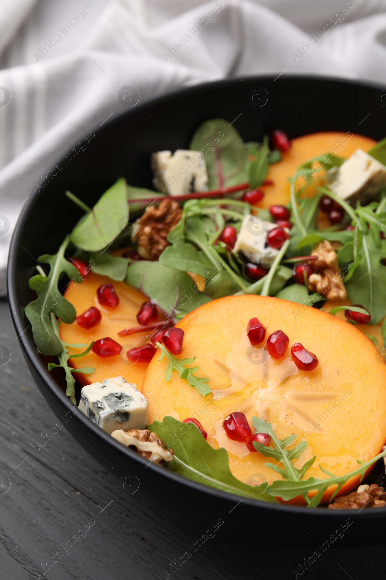 Photo of Tasty salad with persimmon, blue cheese, pomegranate and walnuts served on wooden table, closeup