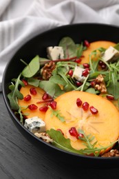 Photo of Tasty salad with persimmon, blue cheese, pomegranate and walnuts served on wooden table, closeup