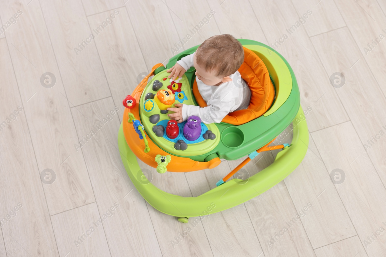 Photo of Cute baby in walker on wooden floor, above view