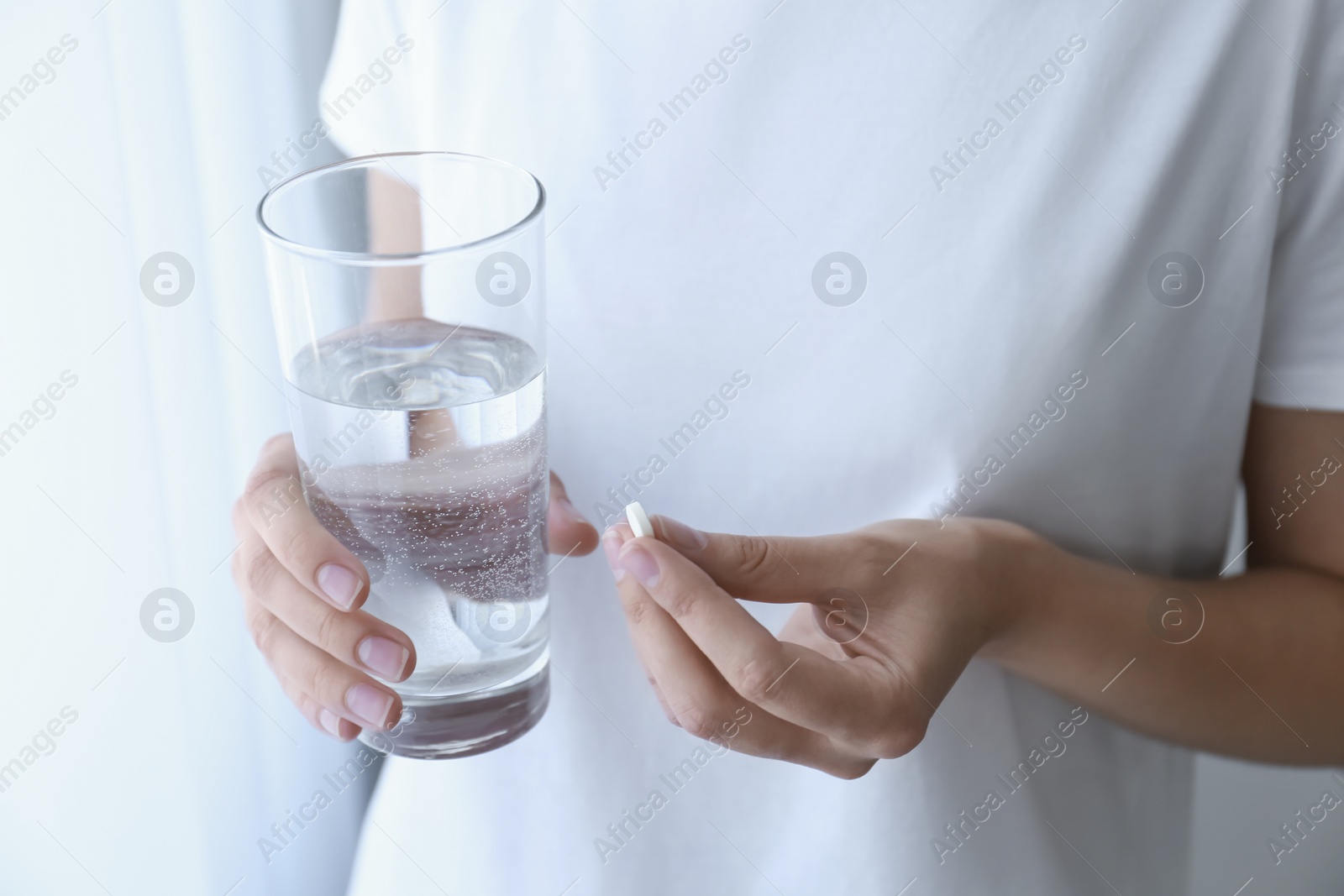 Photo of Woman holding glass of water and pill near window at home, closeup