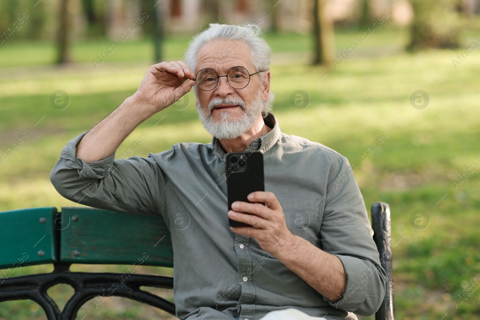 Photo of Portrait of happy grandpa with glasses using smartphone on bench in park