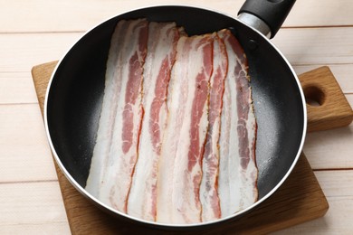 Slices of raw bacon in frying pan on wooden table, closeup