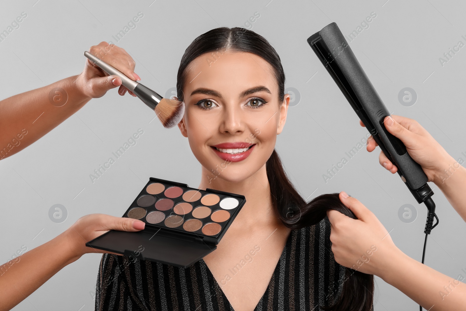 Photo of Makeup artist and hairdresser working with beautiful woman on light grey background
