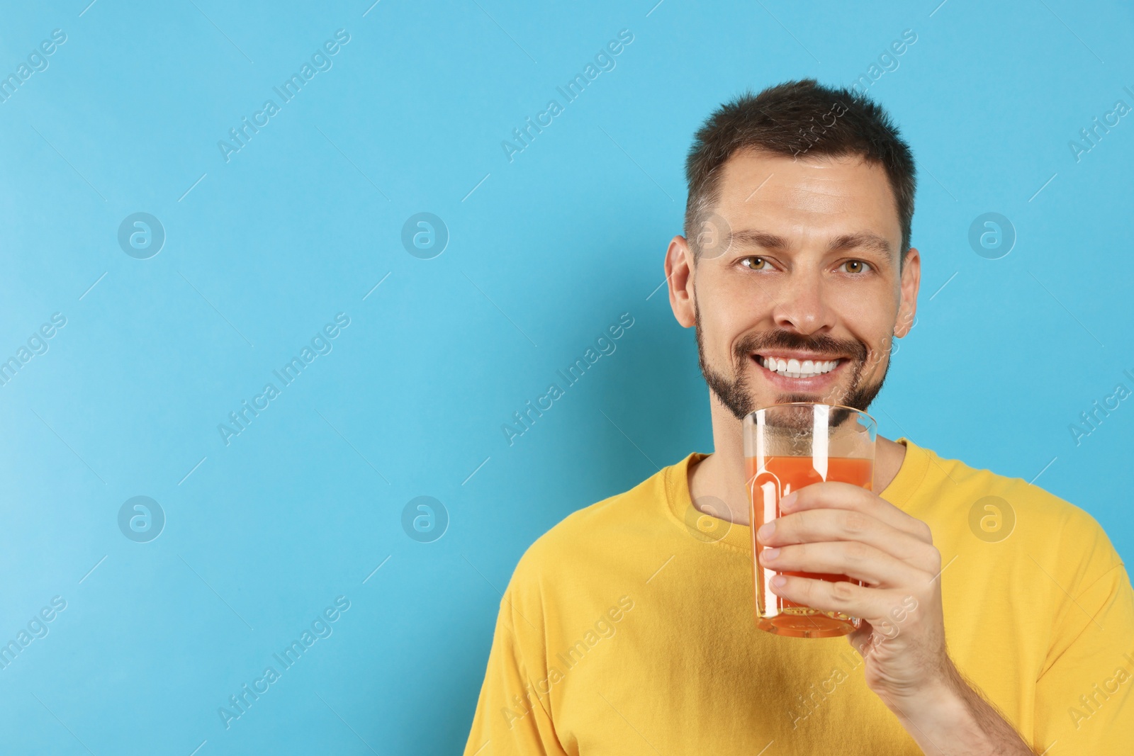 Photo of Man drinking delicious juice on light blue background, space for text