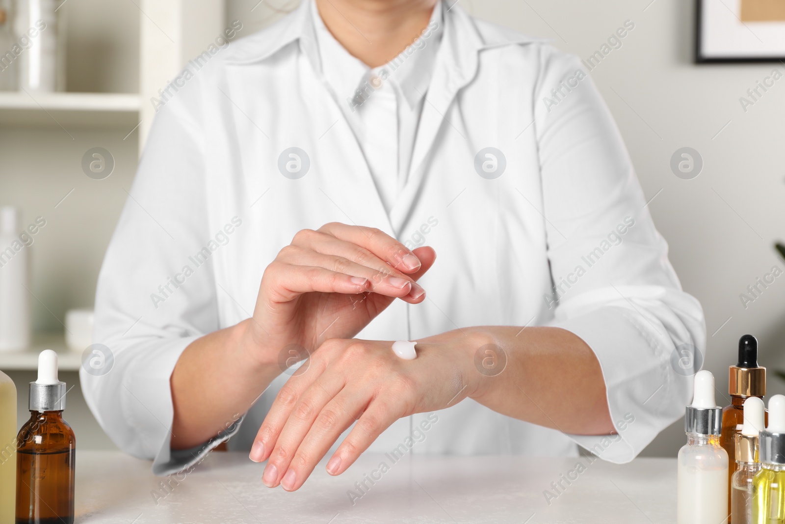 Photo of Dermatologist testing cosmetic product at white table indoors, closeup