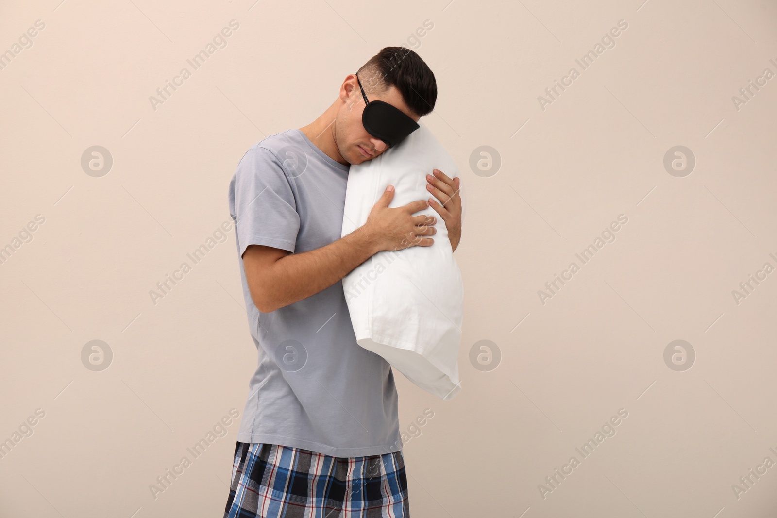 Photo of Somnambulist in eye mask with soft pillow on beige background, space for text. Sleepwalking