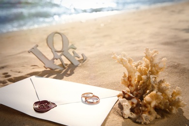 Photo of Envelope, gold wedding rings and coral on sandy beach