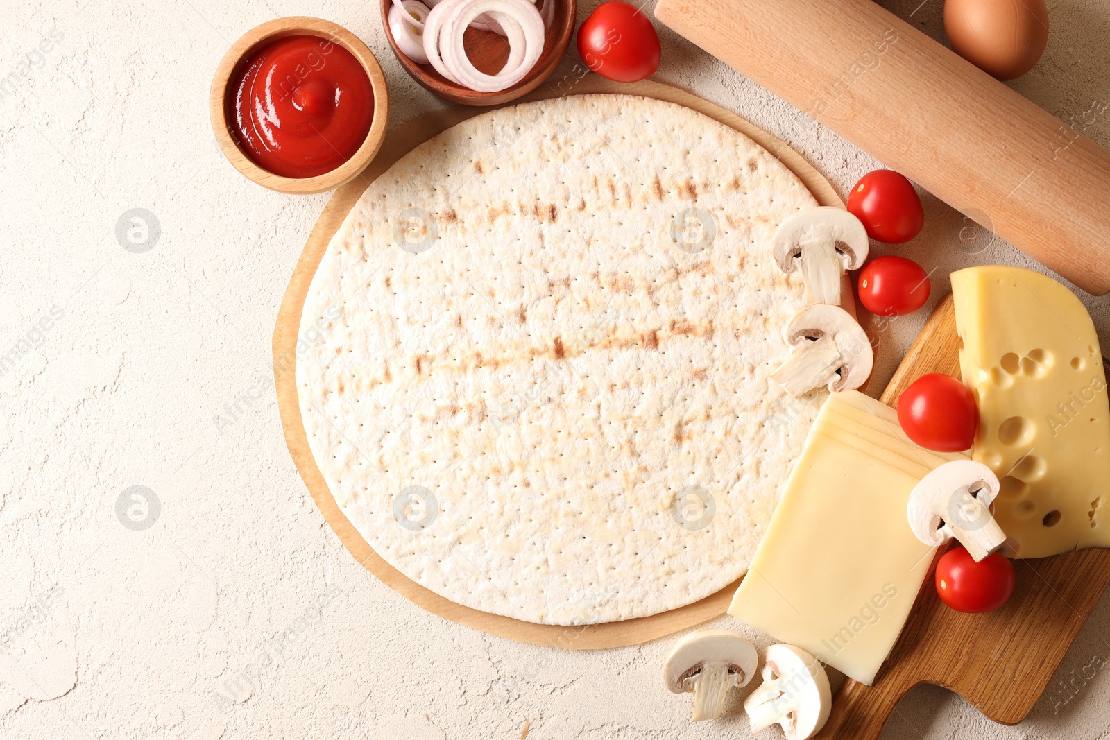 Photo of Pizza base, ketchup and products on light textured table, flat lay. Space for text