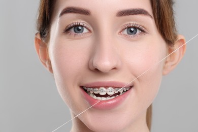 Photo of Smiling woman with braces cleaning teeth using dental floss on grey background, closeup