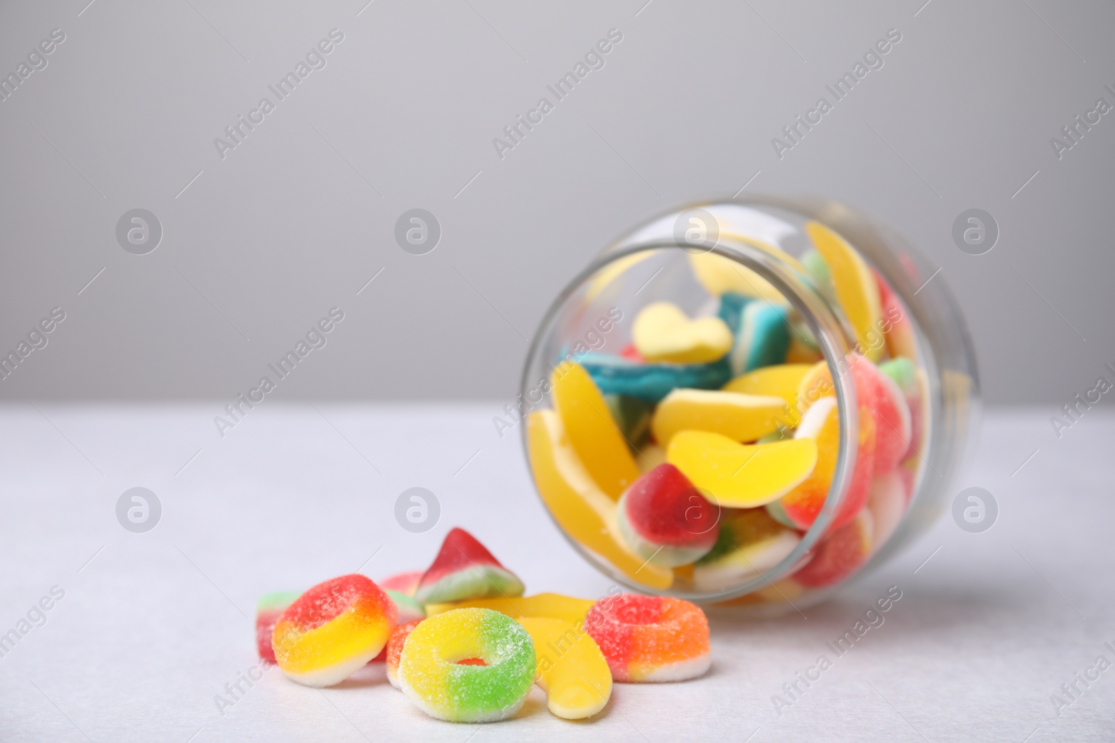 Photo of Tasty jelly candies and jar on light grey table, closeup. Space for text