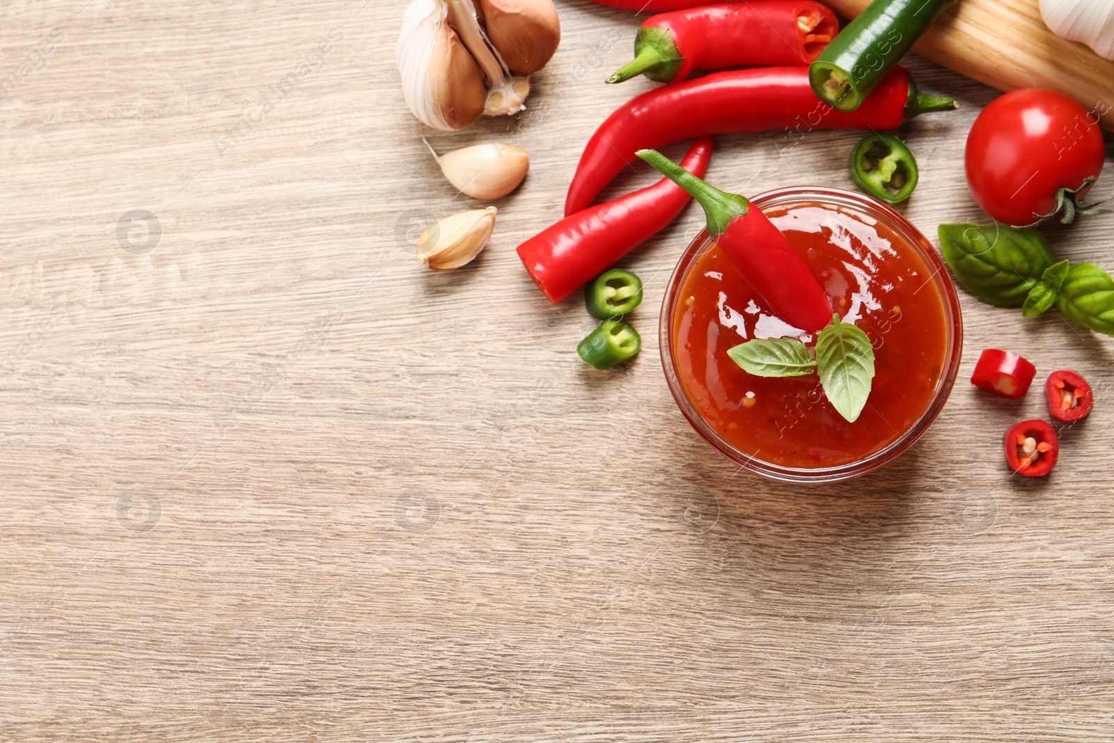 Photo of Spicy chili sauce and ingredients on wooden table, flat lay. Space for text