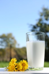 Glass of fresh milk on white wooden table outdoors