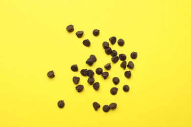 Delicious chocolate chips on yellow background, top view