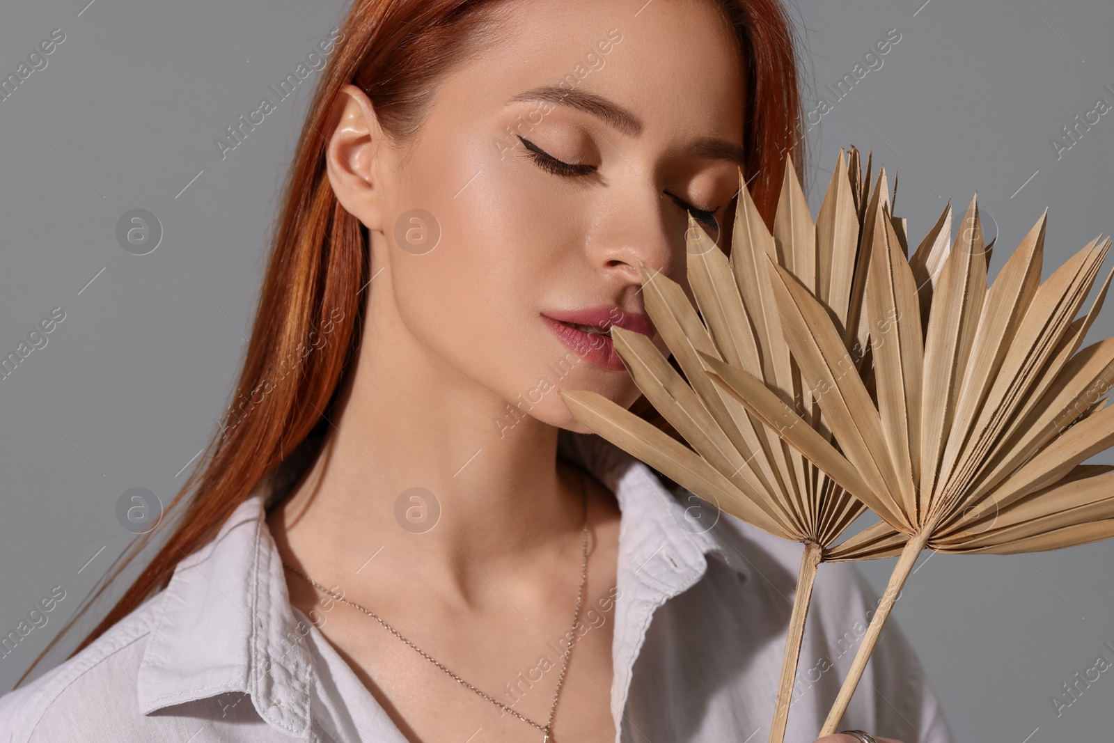 Photo of Beautiful young woman with elegant jewelry and decorative leaves on gray background