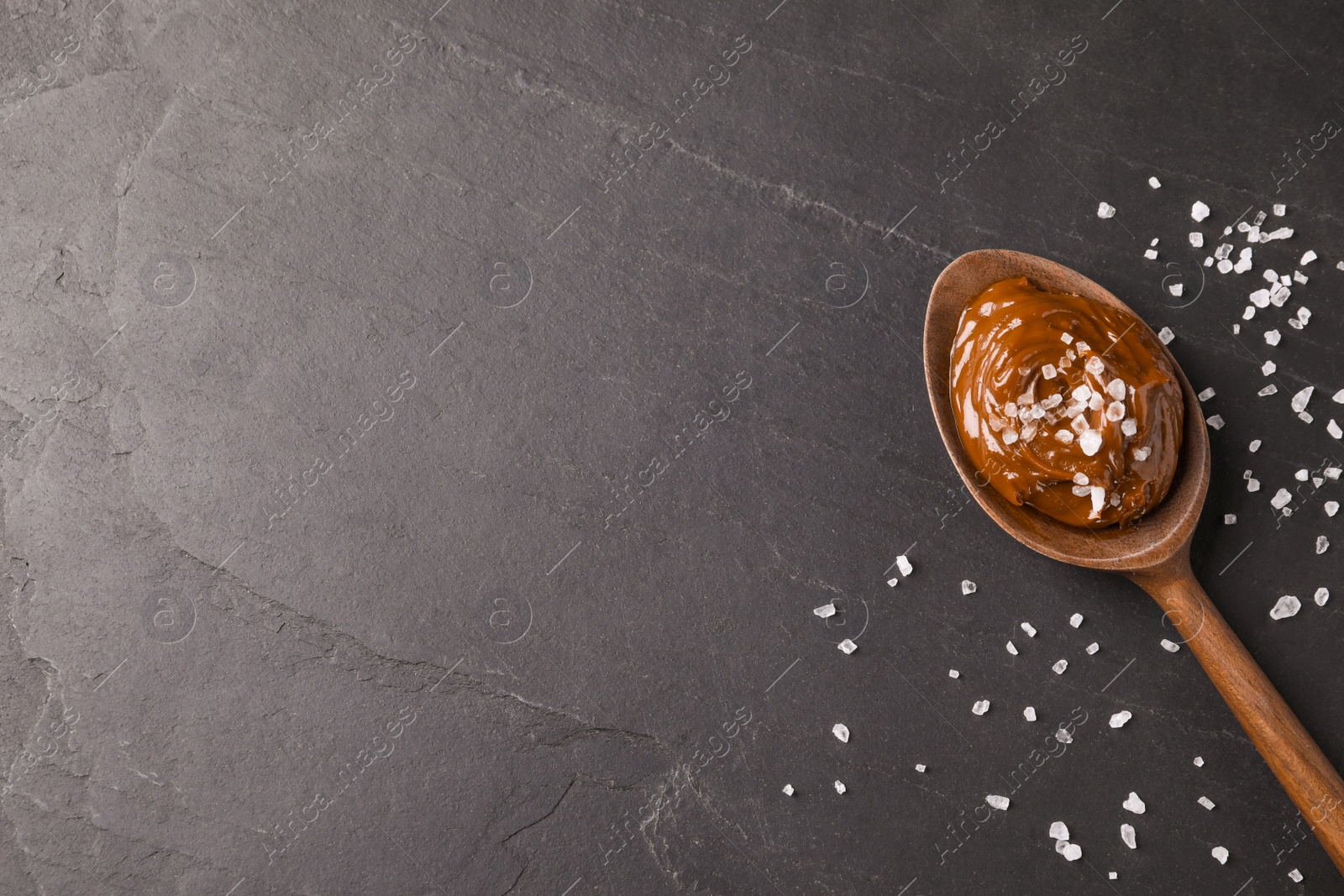 Photo of Salted caramel in spoon on grey table, flat lay. Space for text