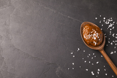 Salted caramel in spoon on grey table, flat lay. Space for text