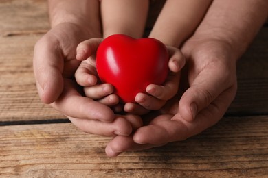 Photo of Father and his child holding red decorative heart at wooden table, closeup