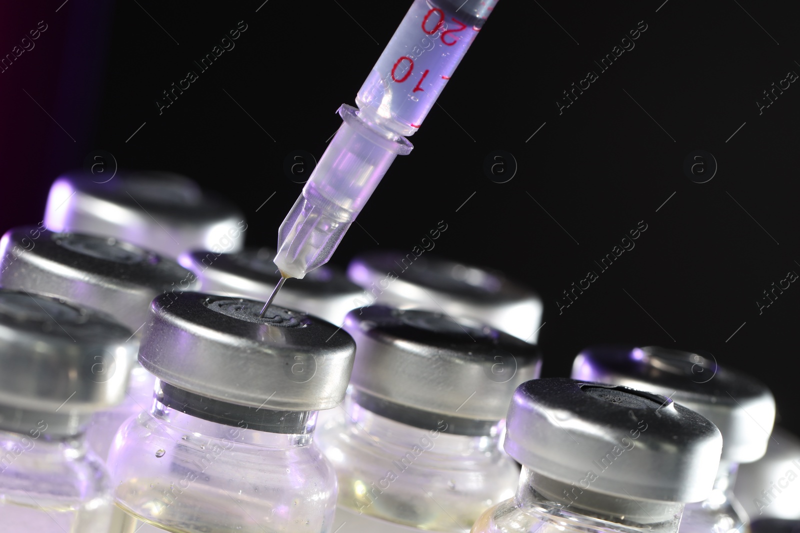 Photo of Filling syringe with medicine from vial against dark background, closeup