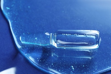 Photo of Pharmaceutical ampoule with medication in transparent gel on blue background, closeup