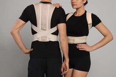 Photo of Closeup view of man and woman with orthopedic corsets on grey background