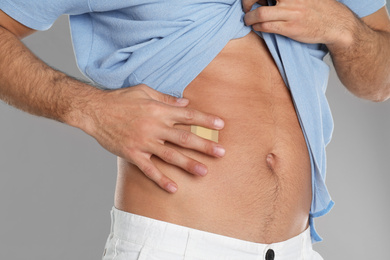 Photo of Man with sticking plaster on tummy against light grey background, closeup