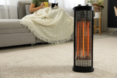 Photo of Woman with cat at home, focus on electric halogen heater, closeup