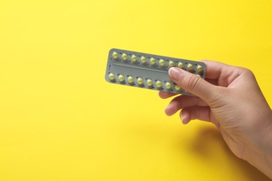 Woman holding birth control pills on yellow background, closeup. Space for text