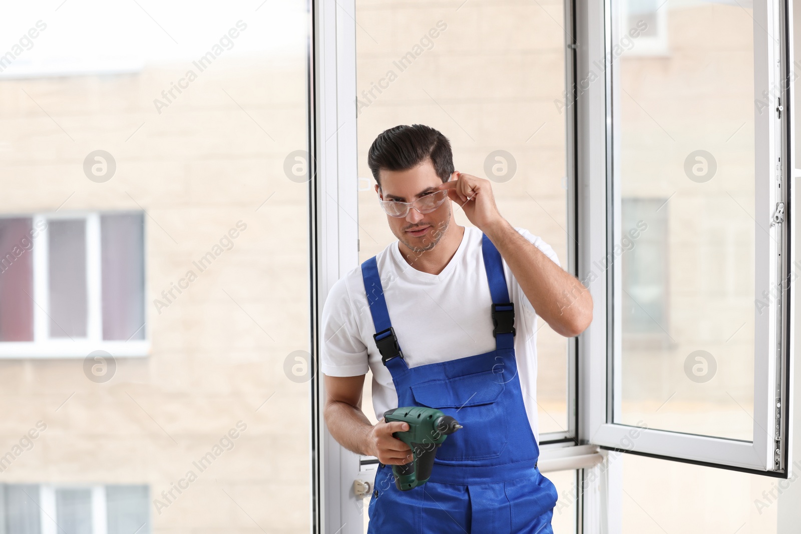 Photo of Repairman with electric screwdriver near plastic window indoors