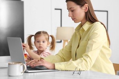 Woman working remotely at home. Mother using laptop while daughter playing at desk