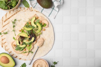 Photo of Tortilla with hummus and vegetables on white table, flat lay. Space for text