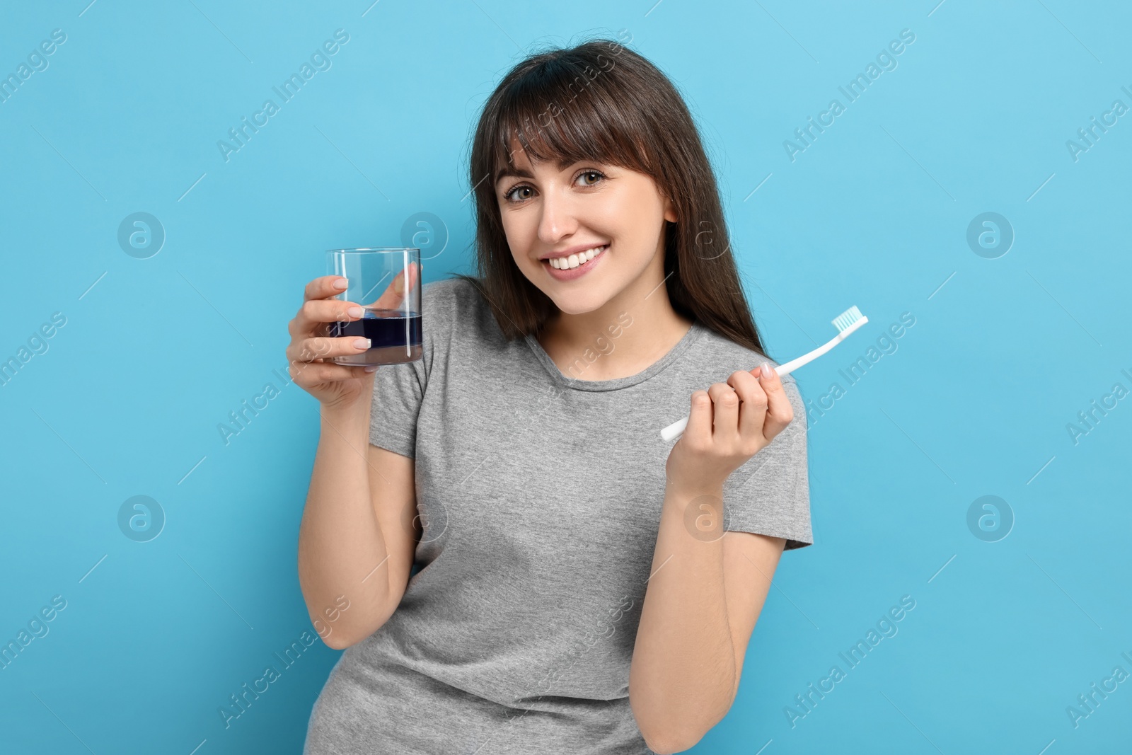 Photo of Young woman with mouthwash and toothbrush on light blue background