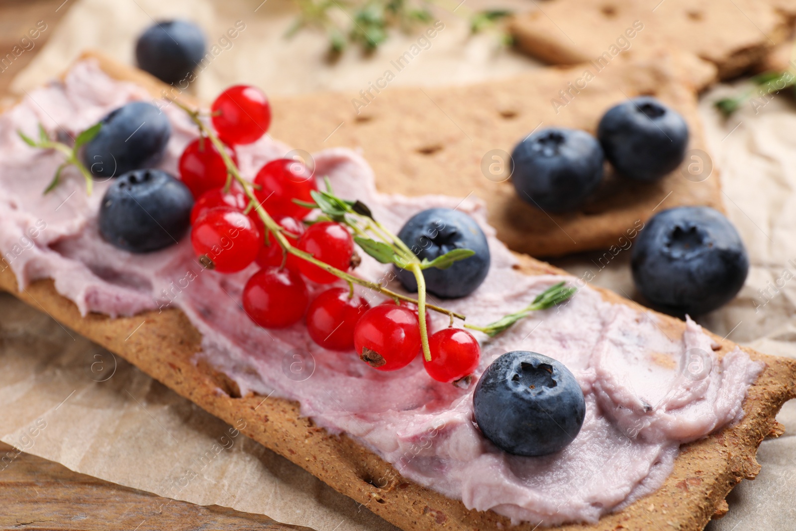 Photo of Tasty crispy crackers with cream cheese, thyme and berries, closeup